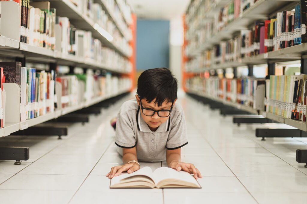 Smart school boy reading a book at the library